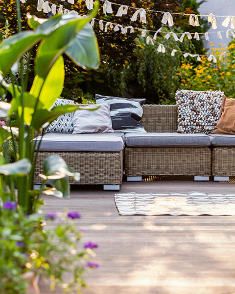 Cozy outdoor seating area with decorative cushions, surrounded by lush greenery and string lights, ideal for relaxation in a garden setting.