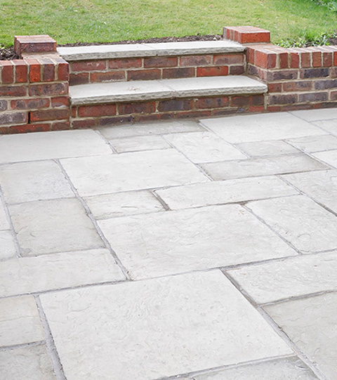 Paved outdoor area featuring light-colored stone slabs and brick steps leading to a grassy area.